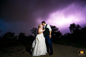 Bride and groom pose outside the Wellshire Event Center, Denver, with a dramatic lightning storm in the background.